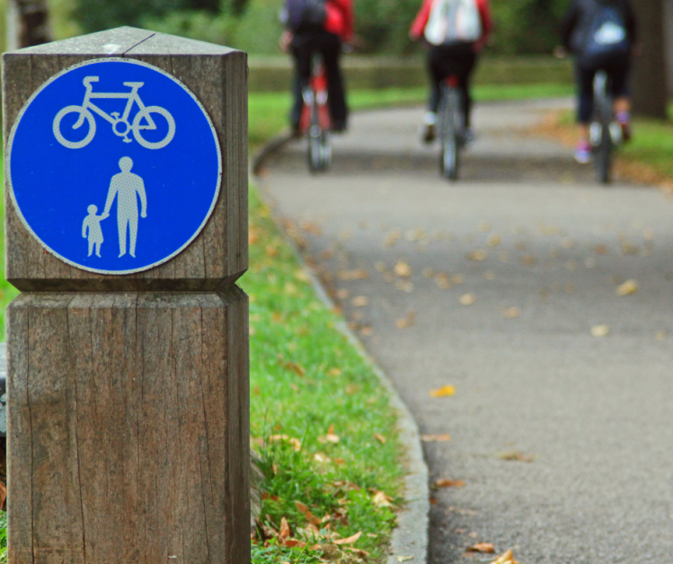 Close up of a blue sign for cycling and pedestrians. Three blurry cyclists in the background