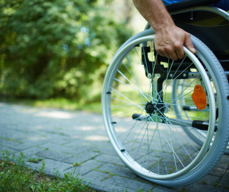 Close up of hand holding onto wheel of a wheelchair sitting on a narrow path